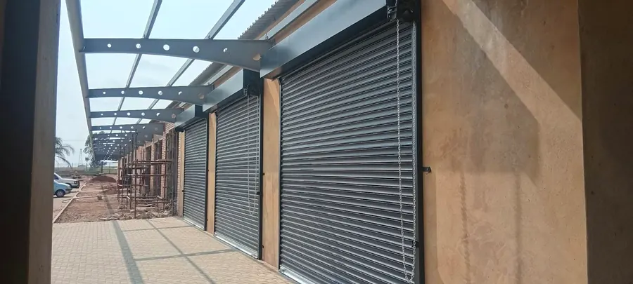 Row of charcoal roller shutter doors under a steel canopy at a new retail centre