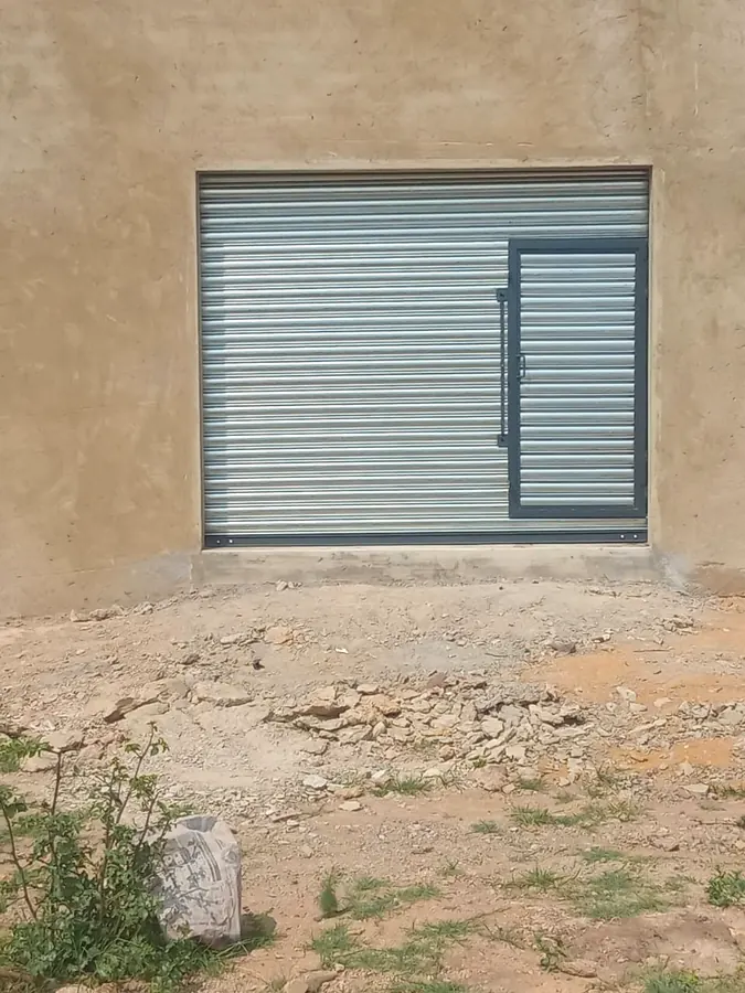 Charcoal roller shutter with side personnel door in a plastered wall